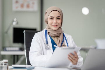 Portrait of Muslim middle age female doctor with head scarf in white lab coat and stethoscope while...