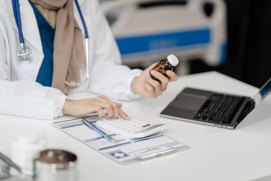 Portrait of Muslim middle age female doctor with head scarf in white lab coat and stethoscope while consult online in laptop. advice on good mental health management and medical treatment costs.