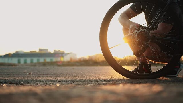 Bicyclist inflates rear flat tire by compact hand pump at sunset, punctured wheel, broken bicycle out of town outside the city. Retractable hose with Schrader inflator chuck connector for valve stem
