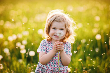 Adorable cute little baby girl blowing on a dandelion flower on the nature in the summer. Happy...