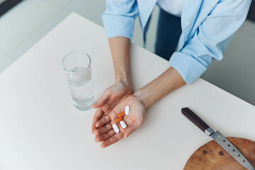 Woman holding pills and water glass next to knife on white table Healthcare concept with medication and hydration