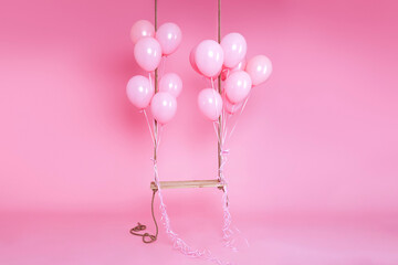 Romantic swing decorated with bunch of pink balloons on a pink background in the studio. Birthday...