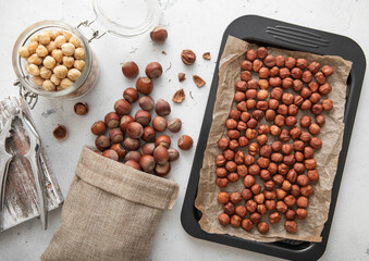 Baking tray with raw hazelnut nuts with cracker and peeled nuts in jar on light kitchen background.Macro.