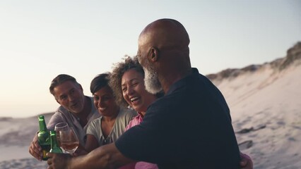 Close up of mature couple with friends sitting on beach looking out to sea at sunset drinking and celebrating with wine and beer - shot in slow motion - Powered by Adobe