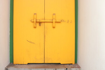 Bright yellow painted antique wood door lock on closed wood door in white cement frame of building in Wat Pho, Bangkok in Thailand.