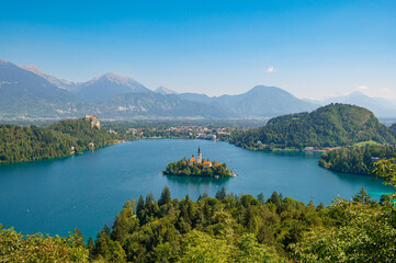 Fototapeta na wymiar View of Lake Bled with St. Marys Church of Assumption on a small island on a sunny day. Lake with turquoise water. Slovenia, Europe. Mountains on background. Areal view from above.
