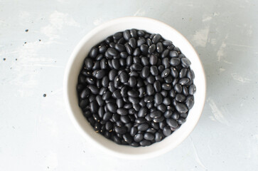 Raw black bens in a white bowl on a gray background. Concept of healthy eating. Vegetarian and vegan food. Horizontal orientation. Top view.