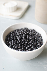 Raw black bens in a white bowl on a gray background. Concept of healthy eating. Vegetarian and vegan food. Vertical orientation. Selective focus