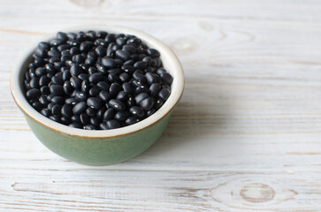 Raw black bens in a green bowl on a white wooden background. Concept of healthy eating. Vegetarian and vegan food. Horizontal orientation. Selective focus. Copy space