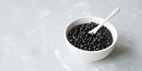 Raw black bens in a white bowl with a teaspoon on a gray background. Concept of healthy eating....