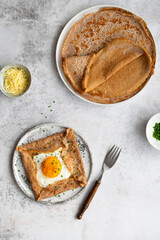 Homemade buckwheat crepes. Galettes Bretonnes with cheese and fried egg on a grey background....