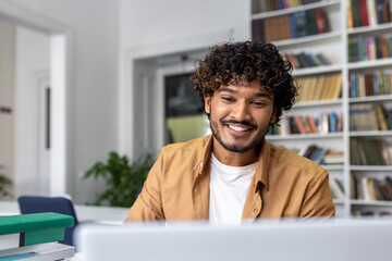 A happy young male professional is engaged in his work on a laptop, smiling in a bright office setting.