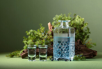 Blue gin in decanter on a background of old snags and juniper branches with berries.