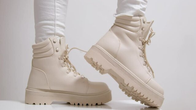 Female pulls and holds the tongue at white boots on tractor soles. Model demonstrating modern autumn footwear.