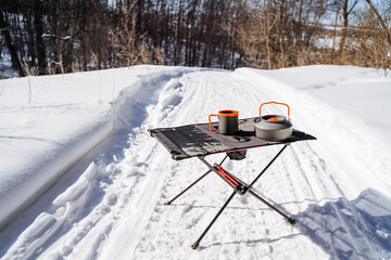 Camping in the woods, dishes on the table, a lightweight compact tourist table, a kettle and a mug.