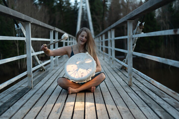 Shaman female playing  shamanic drum on wooden bridge, golden bracelet and rings