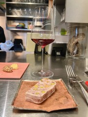 a cup of red wine on a metal table and half a piece of pate on a pink plate
