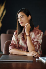 Pensive woman sitting at cafe table with closed laptop in front of her, waiting for business partner