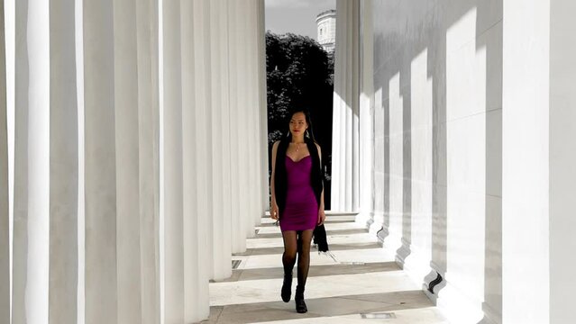 Seductive young woman in dress walking towards camera between symmetrical columns in Vienna, Austria. Slow motion, wide shot.