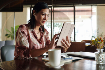 Cheerful businesswoman sitting at cafe table and watching product presentation on tablet