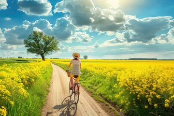 Foto op Canvas person riding a bicycle on a sandy road against the background of a blooming meadow of yellow flowers. © BetterPhoto