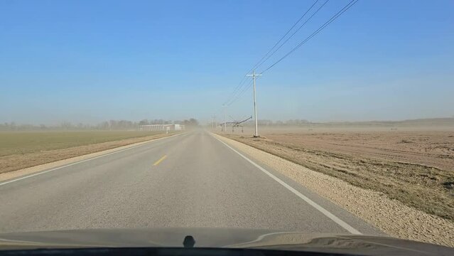 Driving on freeway through small sandstorm created from exposed plowed farm fields on each side of the road after days of drought sunny warm days in the winter season.