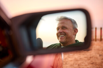 Retired Senior Man Reflected In Mirror Of Classic Open Top Sports Car At Beach Watching Sunrise - obrazy, fototapety, plakaty