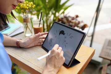 Creative woman drawing sketch on digital tablet when sitting at coffeeshop table