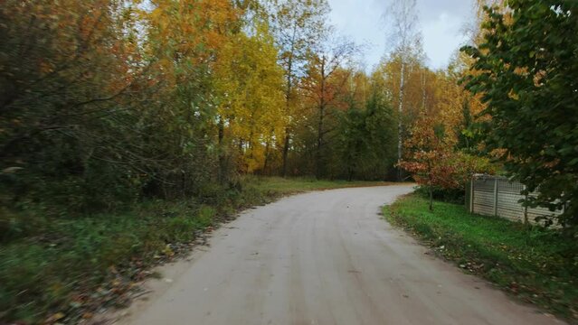 Car is driving on sandy dirt road along autumn forest. View through rear windshield windscreen of car in motion, back glass screen. Travel journey trip in fall. Turns of the unpaved road