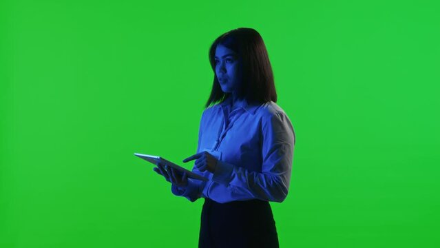 Studio shot of young female data center technician using digital tablet while standing under blue neon light on green chroma key background
