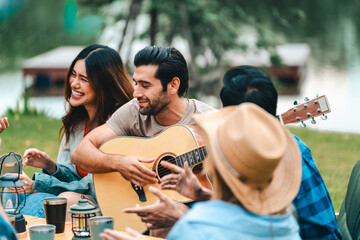 Young friends share a fun summer weekend outdoors with a campfire, bar-b-q, and picnic, celebrating...