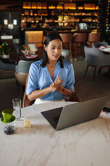 Confident businesswoman talking with colleagues in online meeting when sitting at cafe table