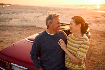 Loving Retired Senior Couple On Vacation Next To Classic Sports Car At Beach Watching Sunrise - 763980157