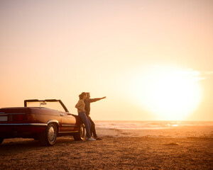 Retired Senior Couple On Vacation Standing By Classic Sports Car At Beach Watching Sunrise
