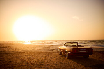 Classic Convertible Sports Car On Shoreline Of Beach At Sunrise