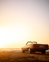 Fototapeta na wymiar Classic Convertible Sports Car On Shoreline Of Beach At Sunrise