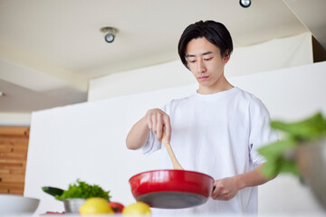 キッチンで料理を作る若い日本人の男性