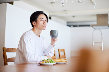 リビングにて朝食を食べる若い日本人の男性