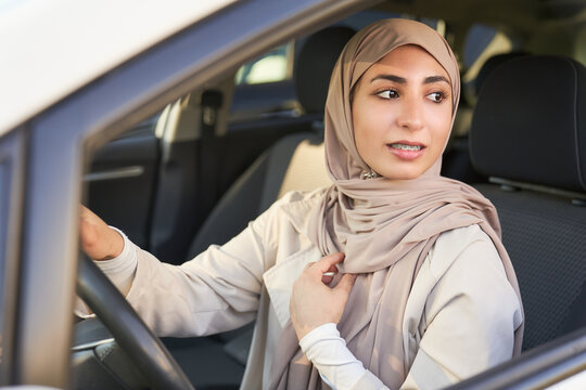 A woman wearing a hijab is driving a car