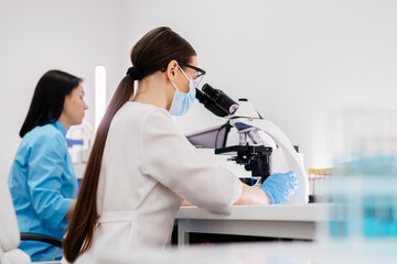 In a modern medical laboratory: a microbiologist in glasses looks under a microscope, analyzing a sample. Scientist working with high-tech equipment. Close-up