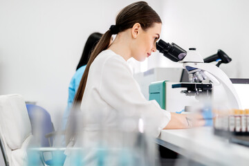 In a modern medical laboratory: a microbiologist in glasses looks under a microscope, analyzing a sample. Scientist working with high-tech equipment. Close-up