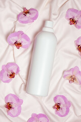 Washing liquid or fabric softener on bed linen with orchid flowers, top view