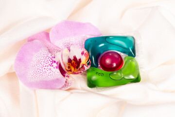 Gel liquid laundry detergent capsule with floral scent with orchid flower on fabric.