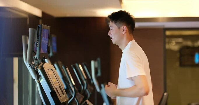 Asian young man running on treadmill in gym. Side view