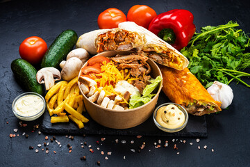 Many pieces of shawarma and Caesar salad and french fries with vegetables on a black background
