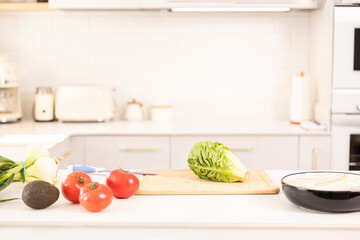 A kitchen counter with a cutting board and a bunch of vegetables including tomatoes, lettuce, and an avocado
