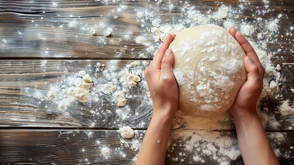Photo sur Plexiglas Pain Hands holding fresh dough on a wooden surface. A person kneads dough, sculpts a form of bread on a wooden table with flour. Pastries, bread making, home baking process. Top view, copy space.