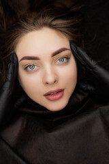 Fototapeta premium Completed work permanent eyebrow makeup girl touches with fingers eyebrows showing the result. Second PMU procedure in a month of permanent eyebrow makeup. Permanent makeup correction.