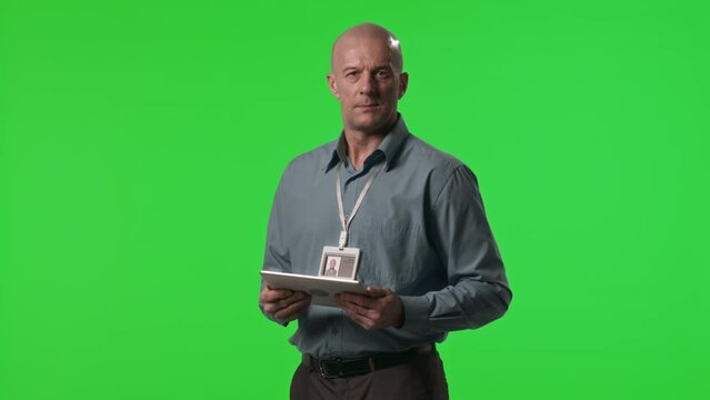 Portrait of mid-aged data center worker using digital tablet and posing for camera against green chroma key wall in studio