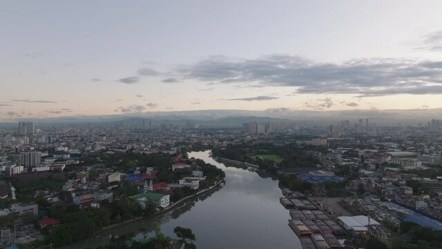 Aerial descending footage of cityscape at sunrise. Calm surface of Pasig river and bulk cargo ships moored at bank. Manila, Philippines